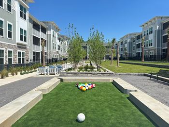 A grassy area with a ball and a row of multicolored balls in front of apartment buildings.